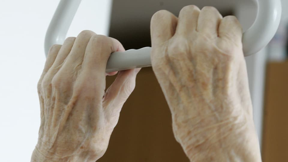 Symbolbild: Zwei Hände eines alten Menschen halten den Griff über dem Spitalbett.