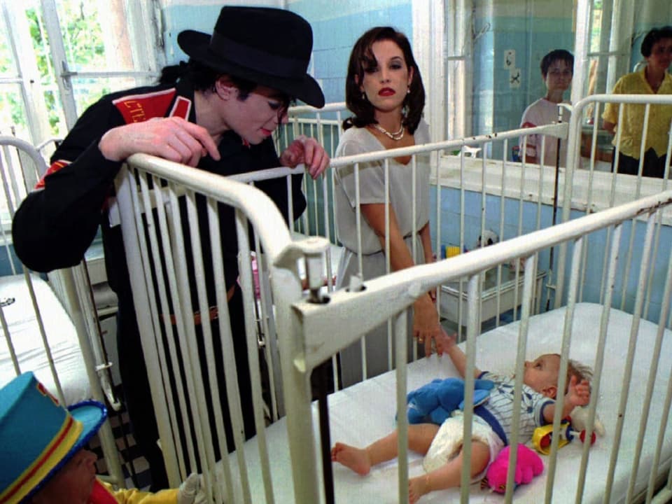 Lisa Marie Presley und Michael Jackson stehen an einem Kinderbett und betrachten ein Baby.