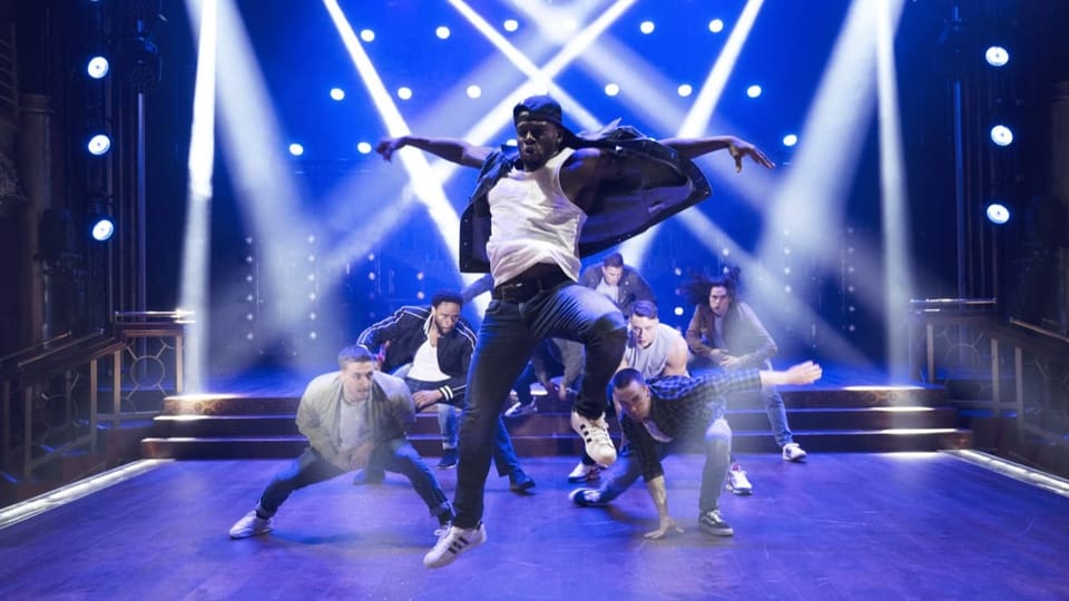 Eine Gruppe junger Männer in Jeans und T-Shirt tanzt auf einer Bühne.