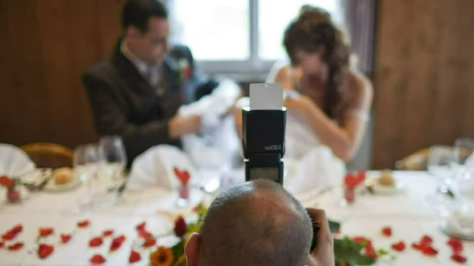 Ein Mann fotografiert ein Hochzeitspaar, welches an einem gedeckten Tisch Platz nimmt.