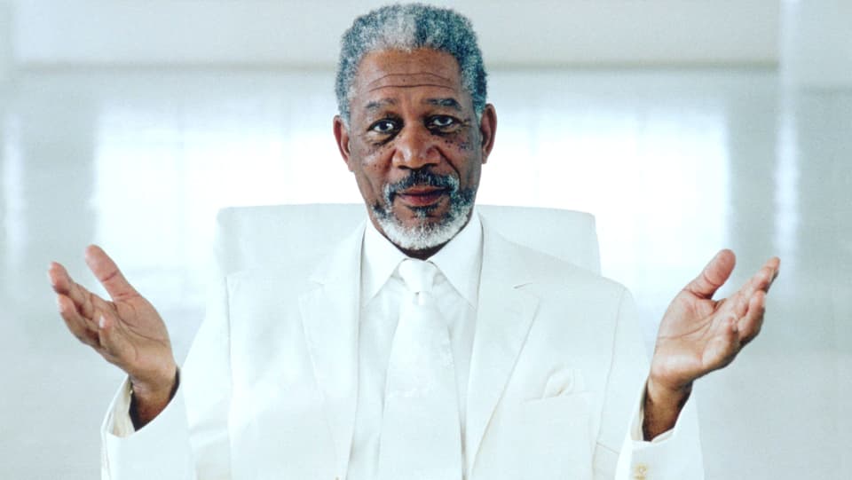 Morgan Freeman in weissem Anzug und mit geöffneten Händen.