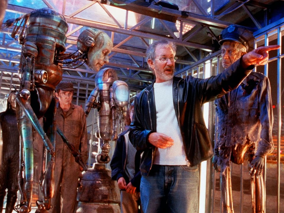 Steven Spielberg gestikuliert auf dem Set umgeben von Robotern in einem Käfig.