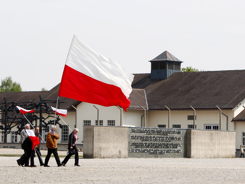 Polnische Bürger laufen durch das ehemalige KZ mit Landesflaggen in den Händen.