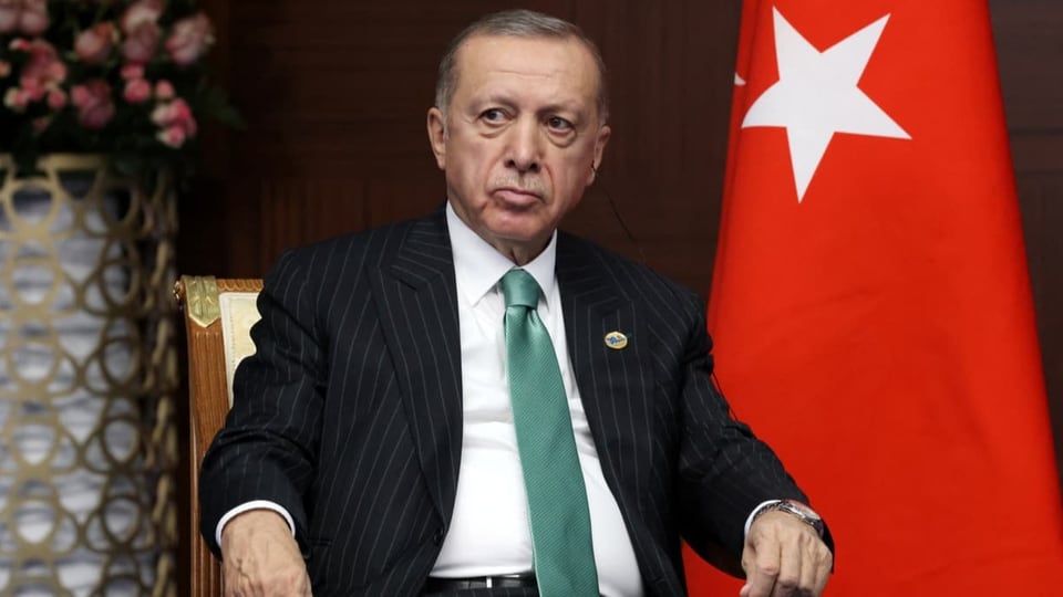 Erdogan sitzt neben einer türkischen Fahne.