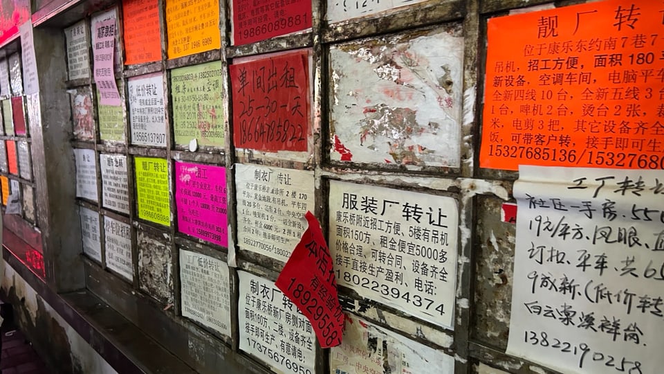 Inserate in chinesischer Schrift hängen an einer Mauer.
