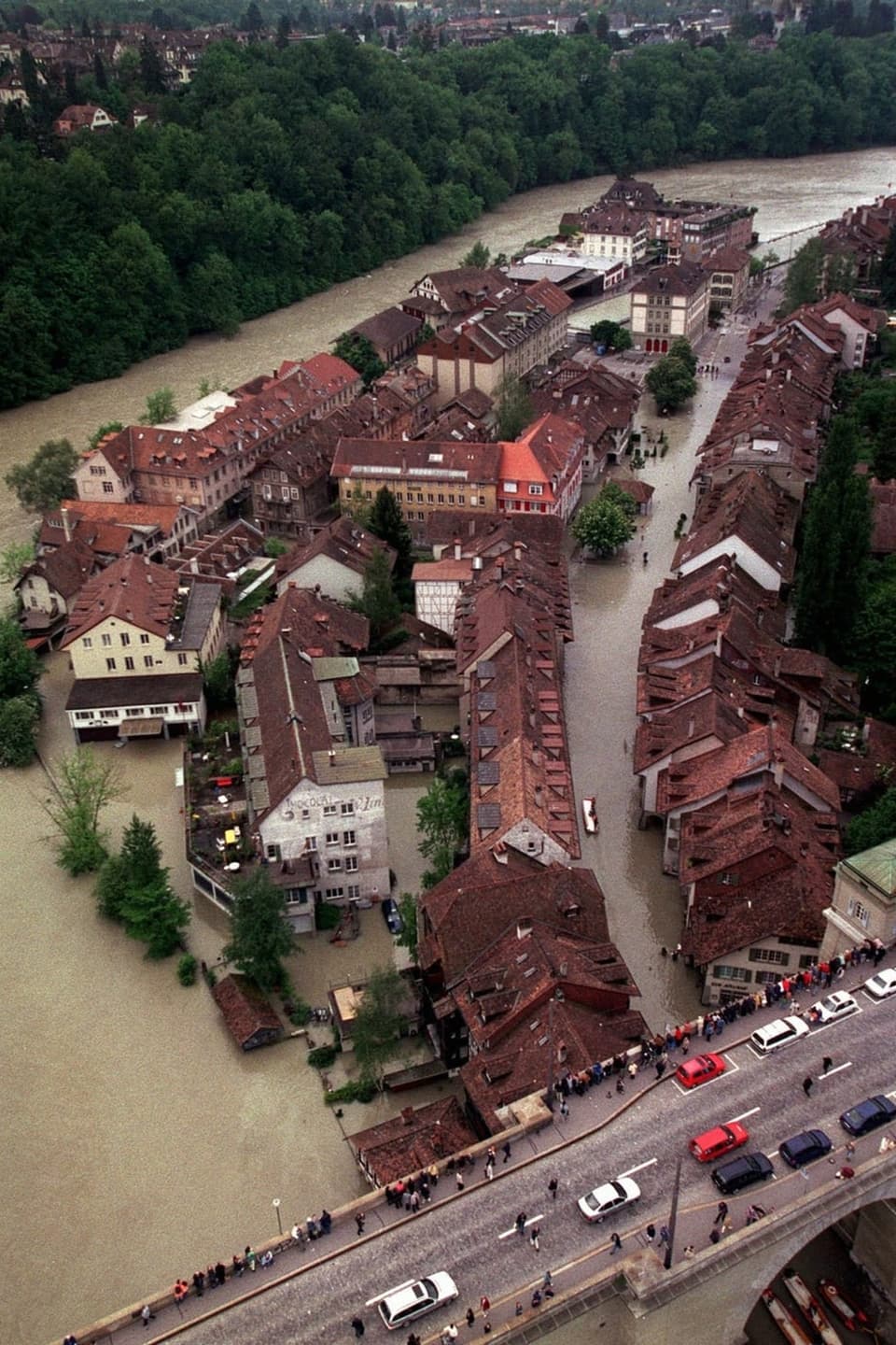 Überschwemmte Stadt mit Häusern und Strassen umgeben von braunem Wasser.