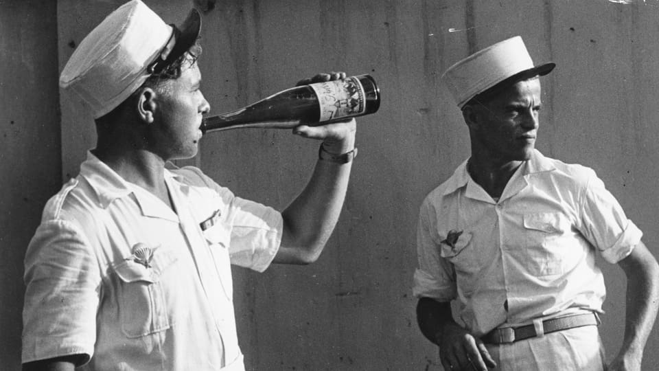 Zwei Soldaten in weisser Ausgangsunifom, einer trinkt Wein aus einer Flasche.