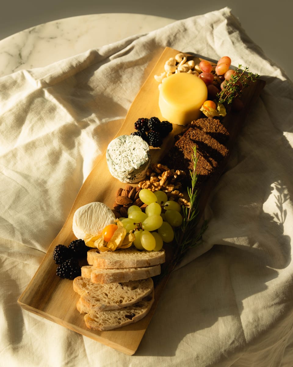 Ein Foto von einer Käseplatte. Darauf sind Früchte, Brot, Nüsse  und verschiedene Arten von veganen Käse.