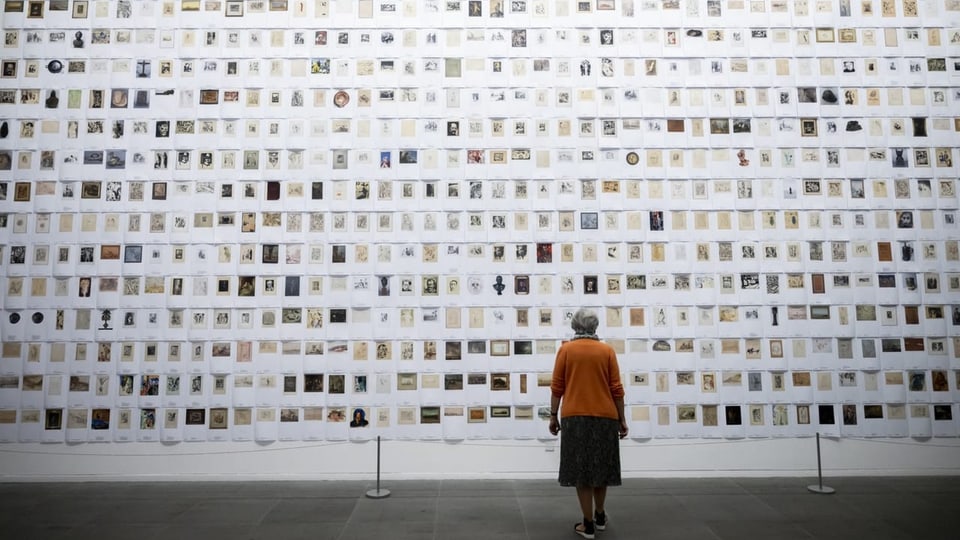 eine Frau steht vor einer Wand voller kleiner Abbildungen.
