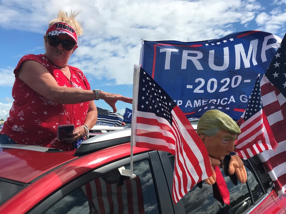 Eine Trump-Anhängerin schaut aus dem mit USA-Flaggen und Trump-Puppe geschmückten Auto.