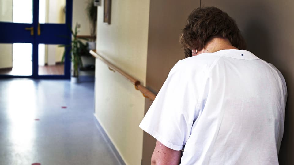 müde, frustrierte Pflegefachfrau lehnt sich in einem Spitalgang an die Wand.