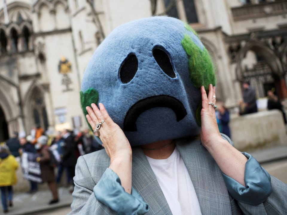 Eine Person mit einer weinenden Maske, die die Erde darstellt.