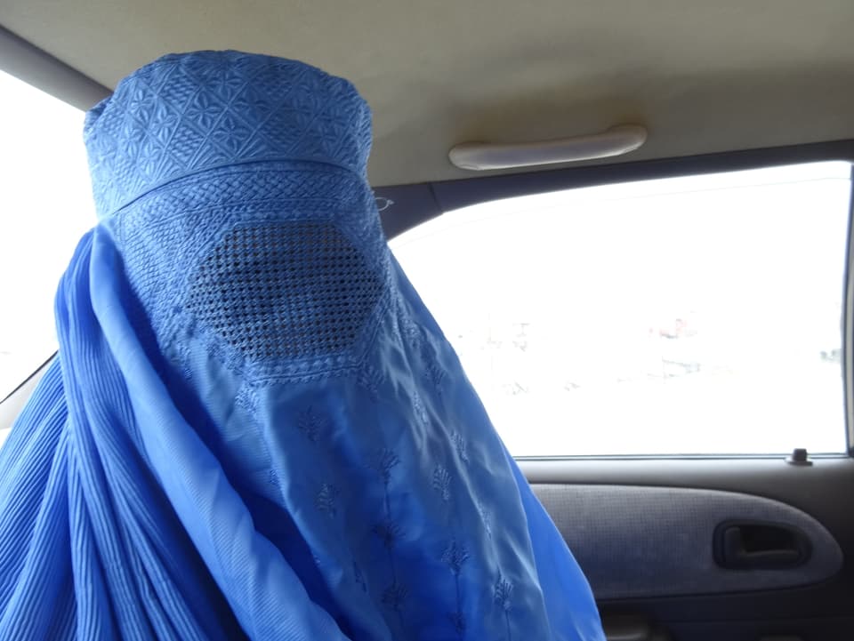 Eine Frau unter einer blauen Burka in einem Auto.