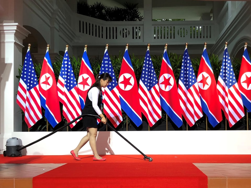 Eine Reinigungskraft vor den Flaggen der USA und Nordkorea.