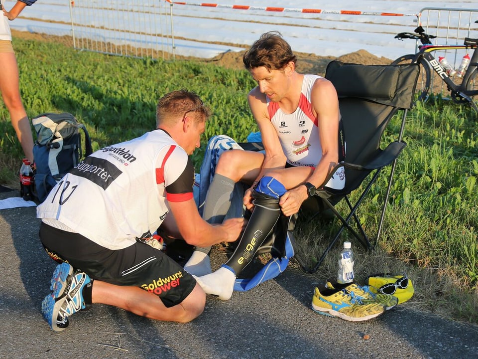 Supporter hilft Athlet in Neoprenanzug. 