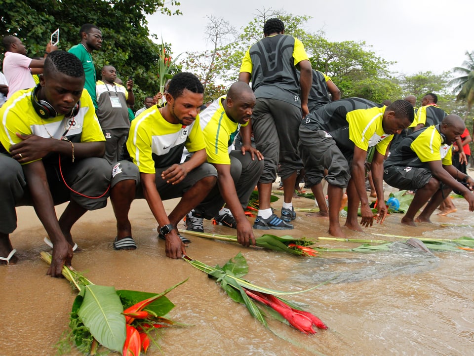 Männer in Sambia legen Blumen am Strand nieder. 