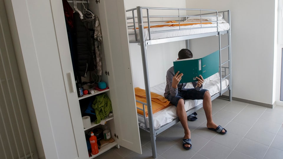 Ein Mann sitzt auf einem Doppelbett und liest