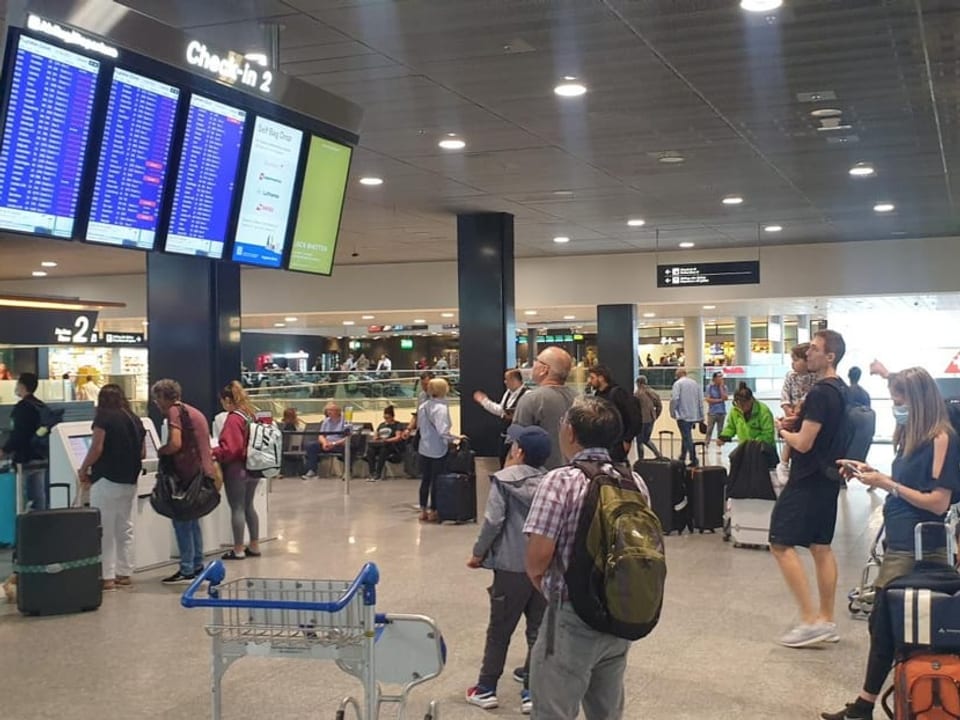Menschen warten am Flughafen Zürich vpr einer Anzeigetafel auf Informationen.