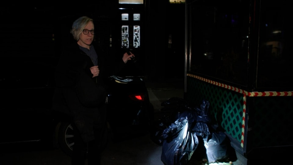 Frau im dunkelt leuchtet auf Abfallsäcke neben überdecktem Holz-Sitzplatz