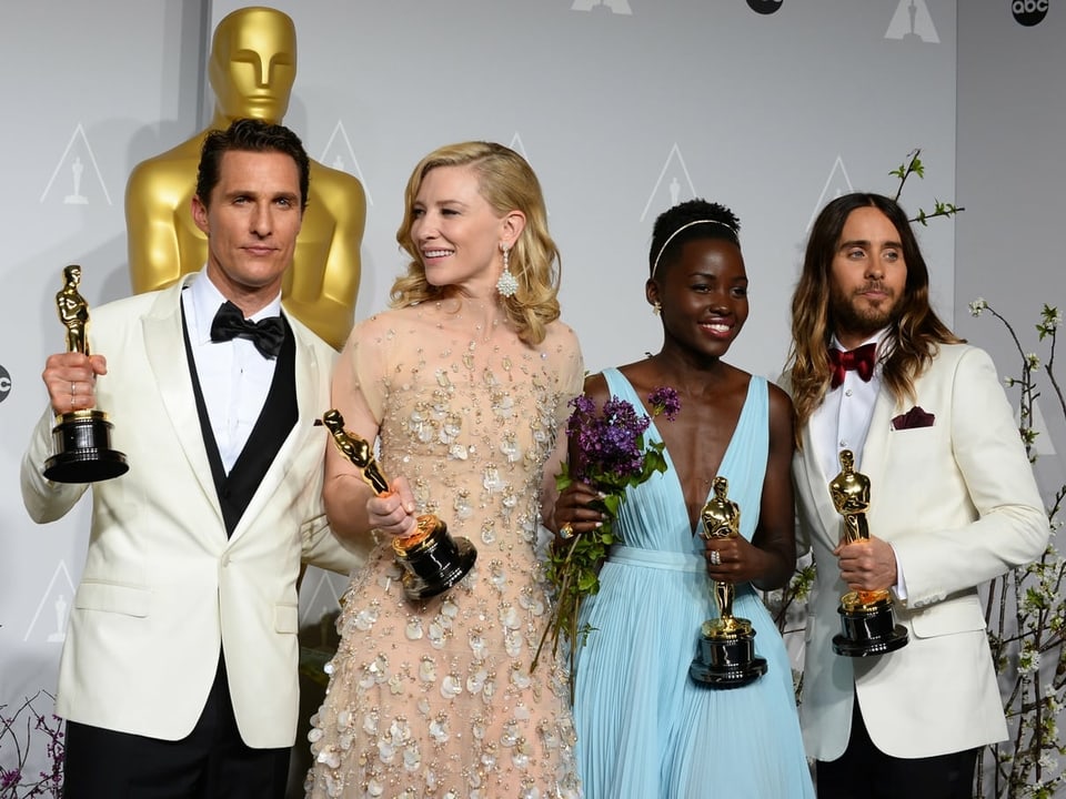 Mann mit Oscarstatue in der Hand, in weissem Sacko, mit anderen Oscarpreisträgern an der Seite
