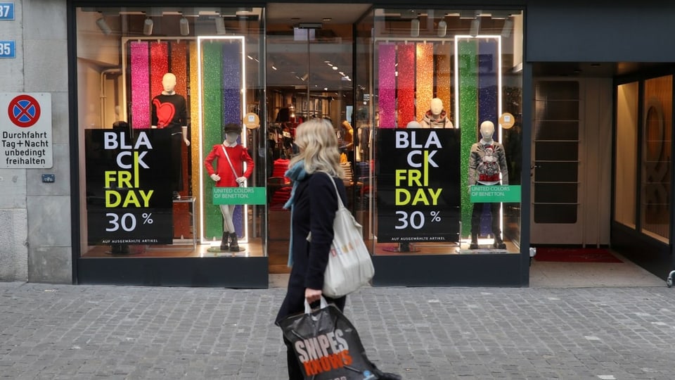 Eine Frau läuft vor einem Kleiderladen vorbei. Bei den Schaufenstern hängen Plakate mit «Black Friday 30 Prozent»