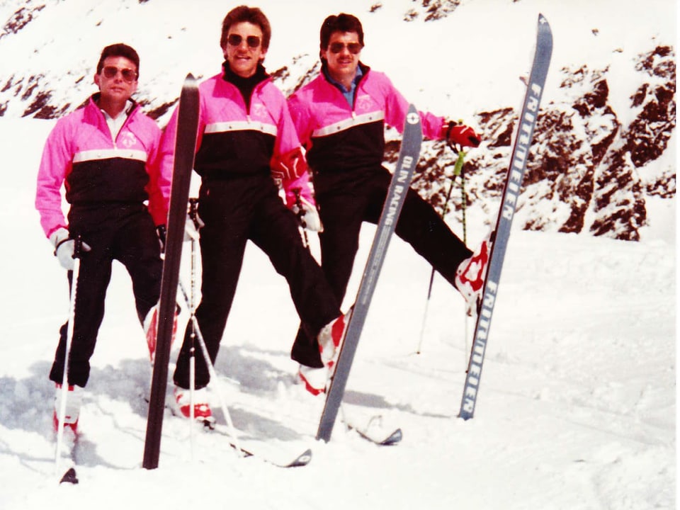 Drei Männer in rosarot-schwarzen Skianzügen.