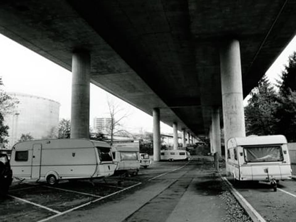 Mehrere Wohnwagen unter einer Brücke, schwarz-weiss.