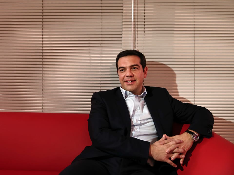 Alexis Tsipras auf einem roten Sofa sitzend.