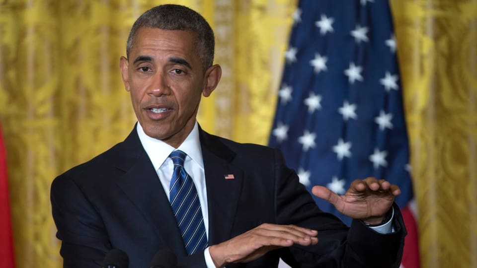 Obama vor einem goldenen Vorhang und US-Flagge mit bestimmtem Blick und gestikulierenden Händen.