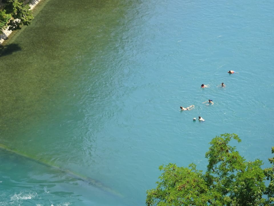 Ein halbes Dutzend Menschen schwimmen in einem Fluss, Aufnahme von oben. 