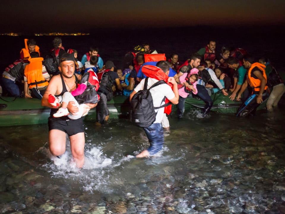 Ein Schlauchboot mit Flüchtlingen kommt an der südöstlichen Küste von Kos an. Ein Mann trägt ein kleines Kind im Arm.