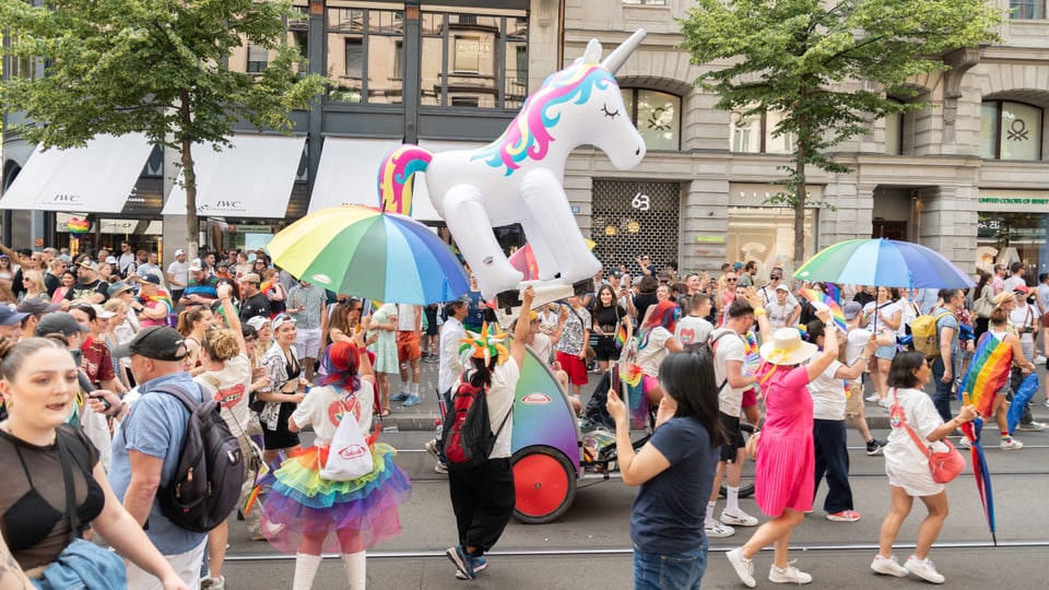 Umzug mit vielen Menschen, LGBTQ+ Fahnen, ein grosser Einhorn-Ballon.
