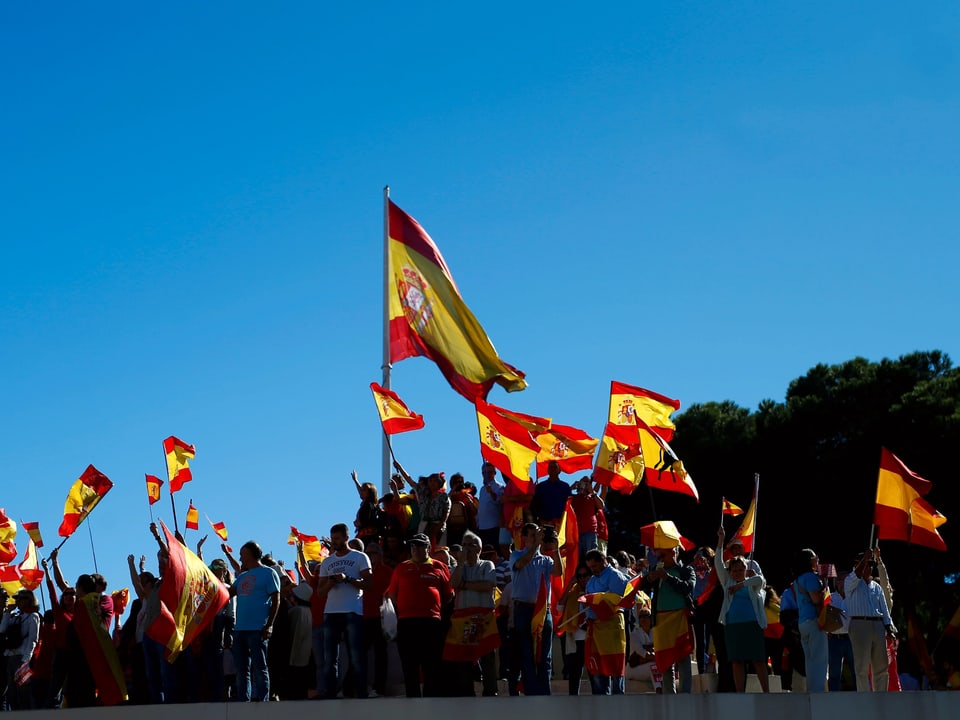 Menschenansammlung und mehrere Spanien-Fahnen vor blauem Himmel.