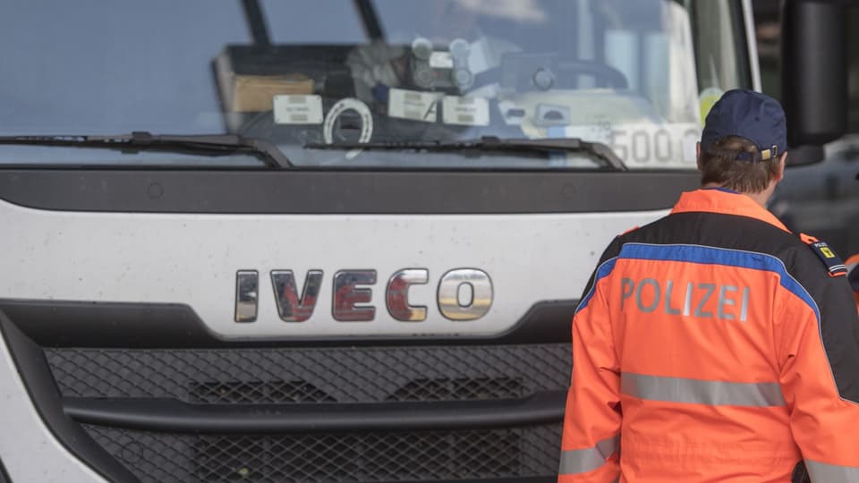 Das Bild zeigt einen Polizisten der Kantonspolizei Uri, der vor einem Lastwagen der Marke Iveco steht.