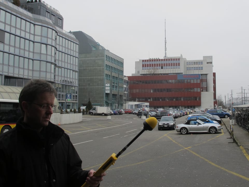 Markus Gugler steht mit dem Messgerät auf dem Parkplatz, im Hintergrund ein grosses Sendemast auf einem Gebäude.