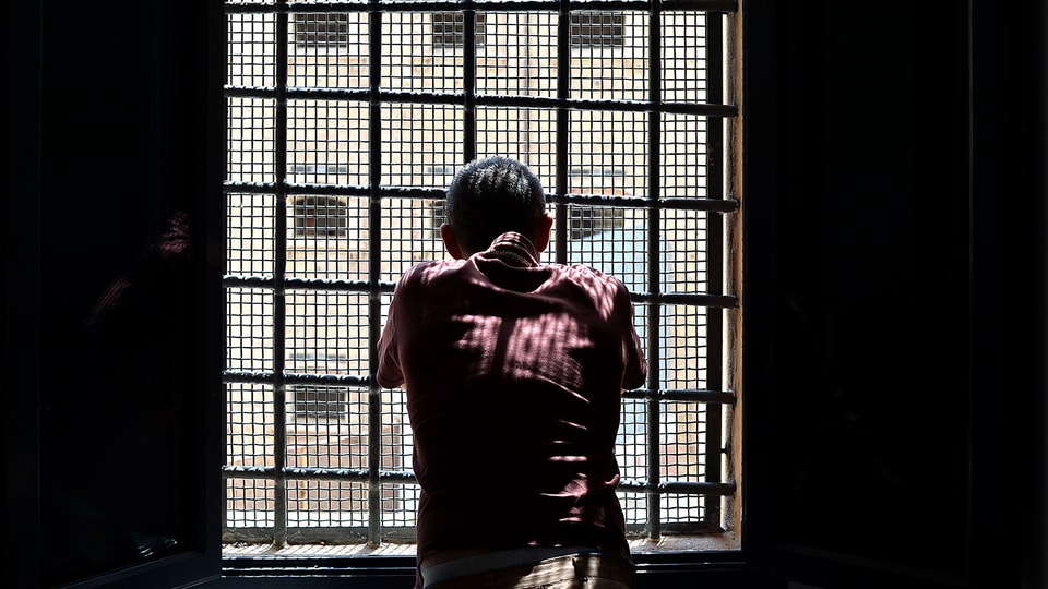 Ein Mann schaut durch ein vergitteretes Gefängnisfenster.