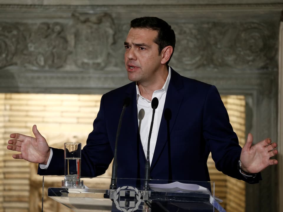 Tsipras steht am Rednerpult und signalisiert mit ausgestreckten Händen seine Offenheit.