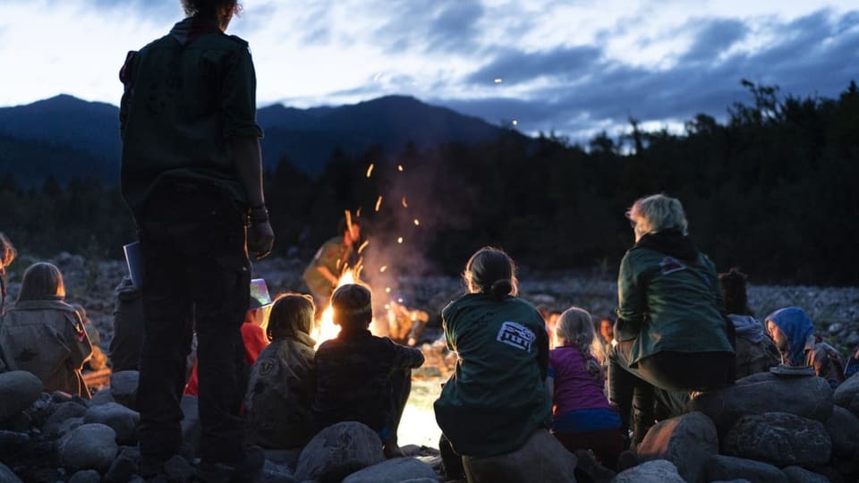Eine Gruppe Pfadfinder sitzt am Abend an einem Lagerfeuer.