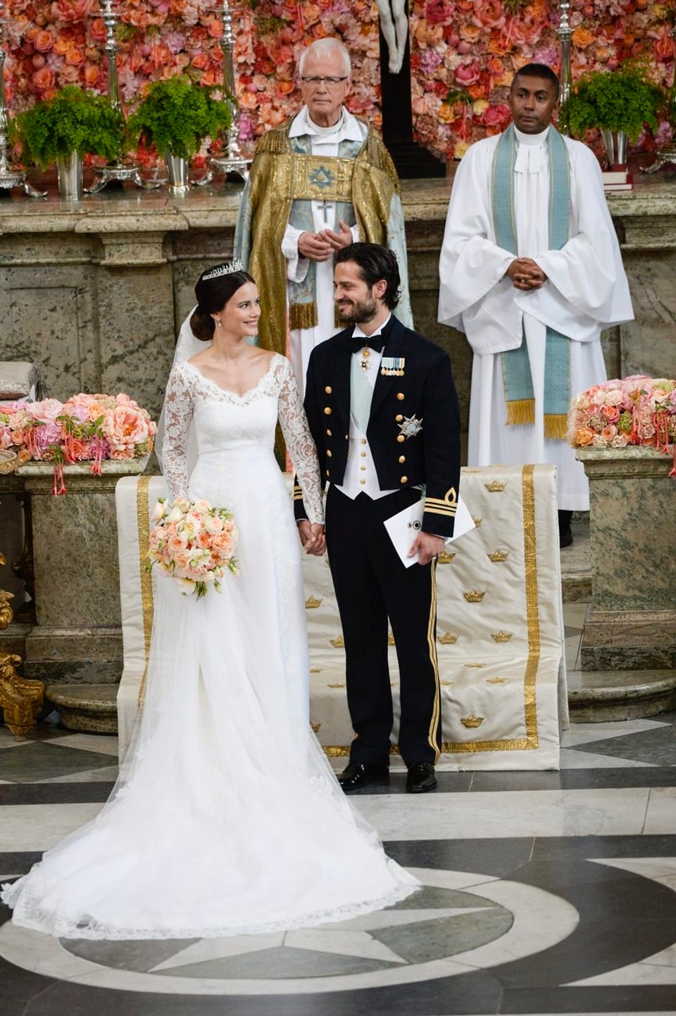 Sofia und Philip Hand in Hand vor dem Altar. Sie mit Blumen in der rechten Hand.