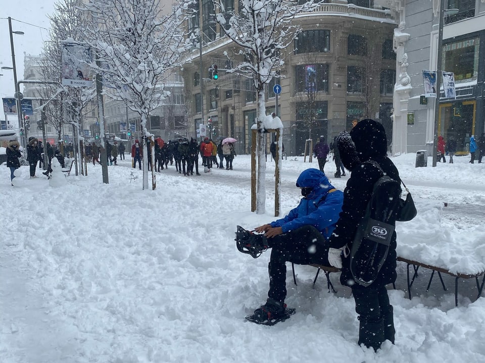Ein Mann zieht sich Schneeschuhe an, dahinter sind viele Fussgänger im Schnee zu sehen.