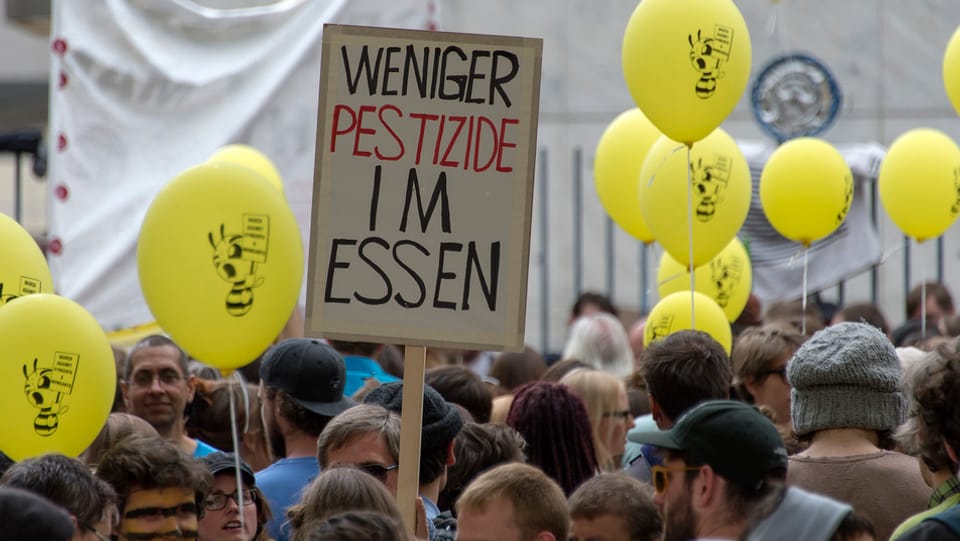 Transparent "Weniger Pestizide im Essen" und Menschenmenge.