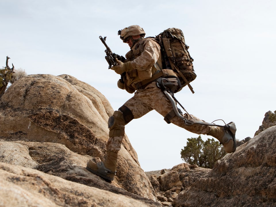 Soldat mit voller Ausrüstung und schwerem Rucksack läuft zügig durch unwegsames Gelände.