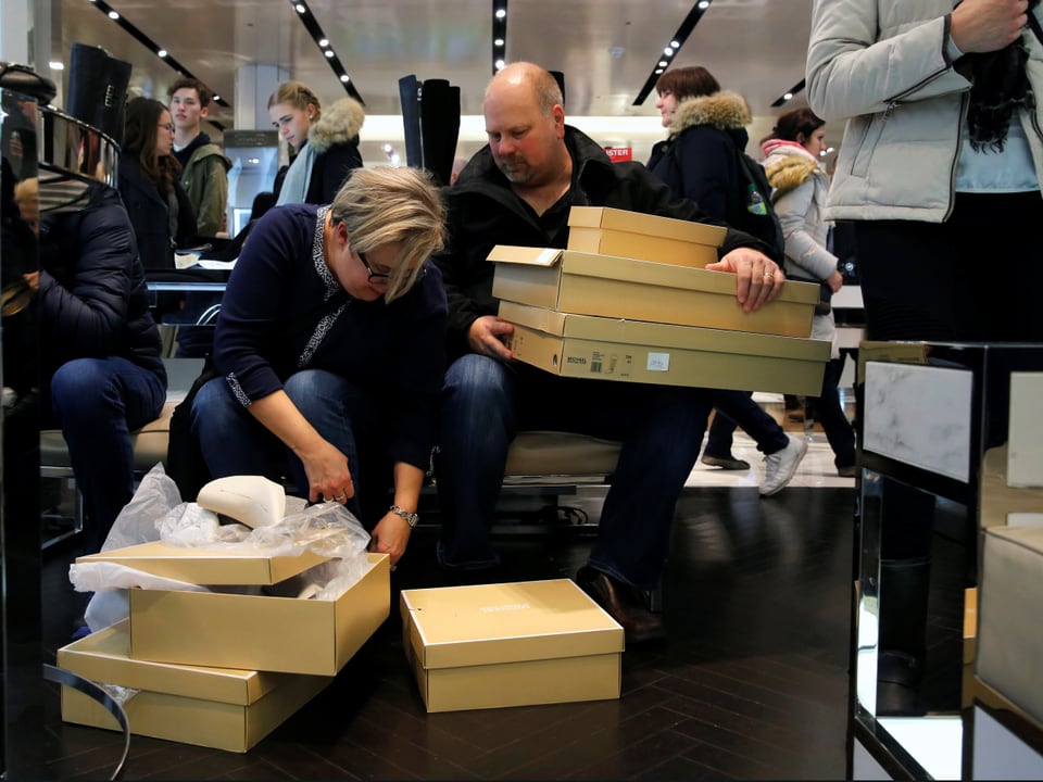 Eine Kunden probiert im New Yorker Kaufhaus Macy's diverse Schuhe. Ihr Mann hält die Kartonschachteln. 