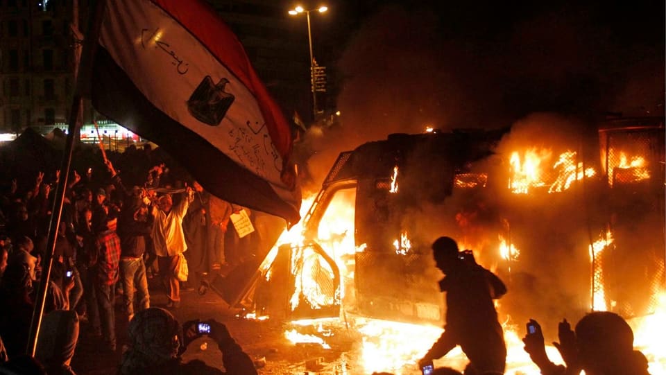 Demonstrierende Menge steht vor brennendem Auto der Sicherheitskräfte in Kairo.