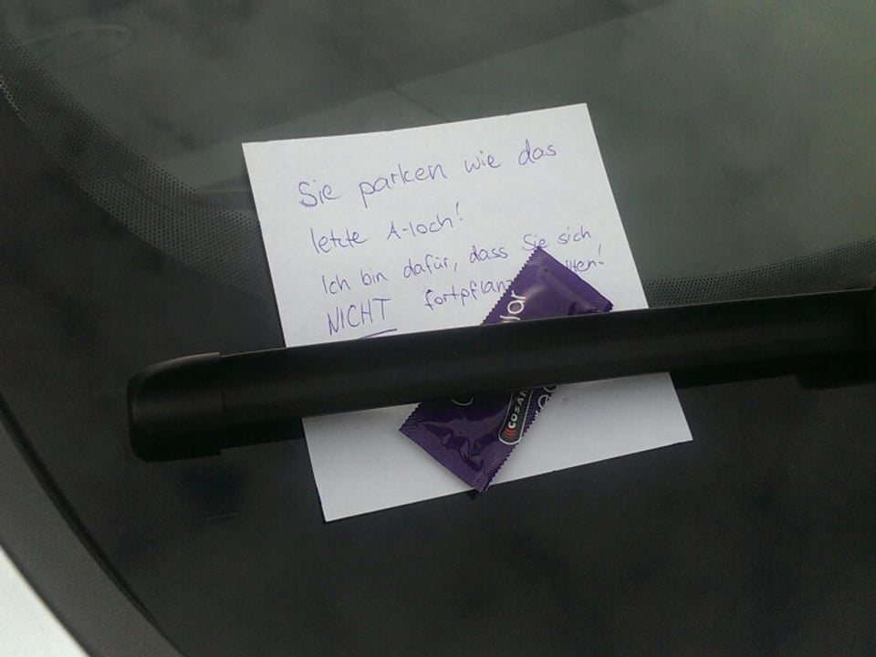 Zettel an der Windschutzscheibe: "Sie parken wie das letzte Arschloch! Ich bin dafür, dass Sie sich nicht fortpflanzen." Daneben liegt ein Kondom.