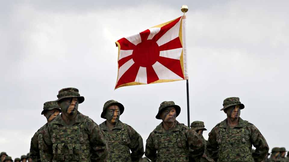 Fünf Soldaten stehen vor der  Flagge der Boden­selbstverteidigungs­streitkräfte.