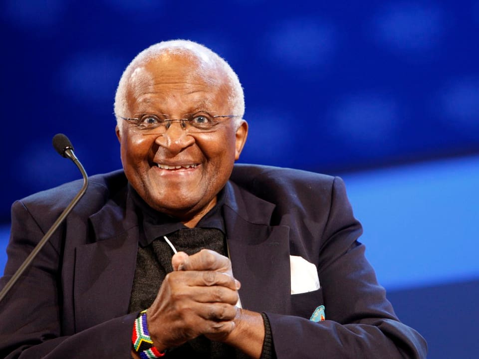 Desmond Tutu hält sich die Hände und lacht