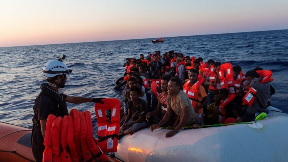 Ein Mitglied der Sea-Watch-Besatzung verteilt Rettungswesten an Migranten auf einem überfüllten Schlauchboot.