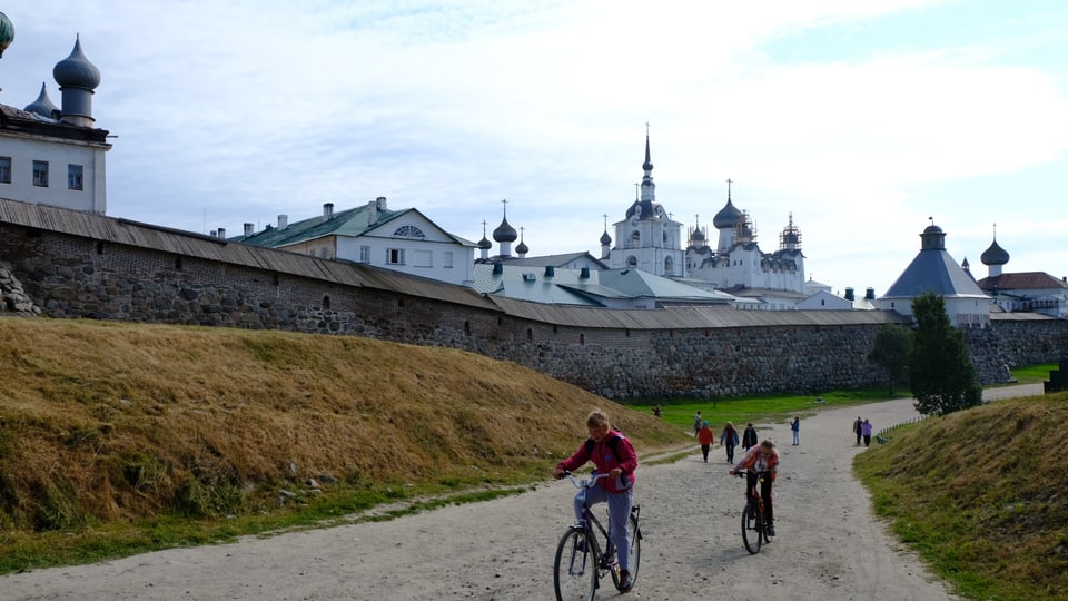 Kinder fahren auf Fahrrädern am Kloster vorbei.