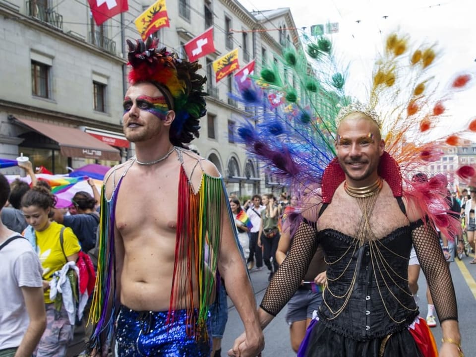 Zwei bunt-gekleidete und händehaltende Männer an der Pride in Genf